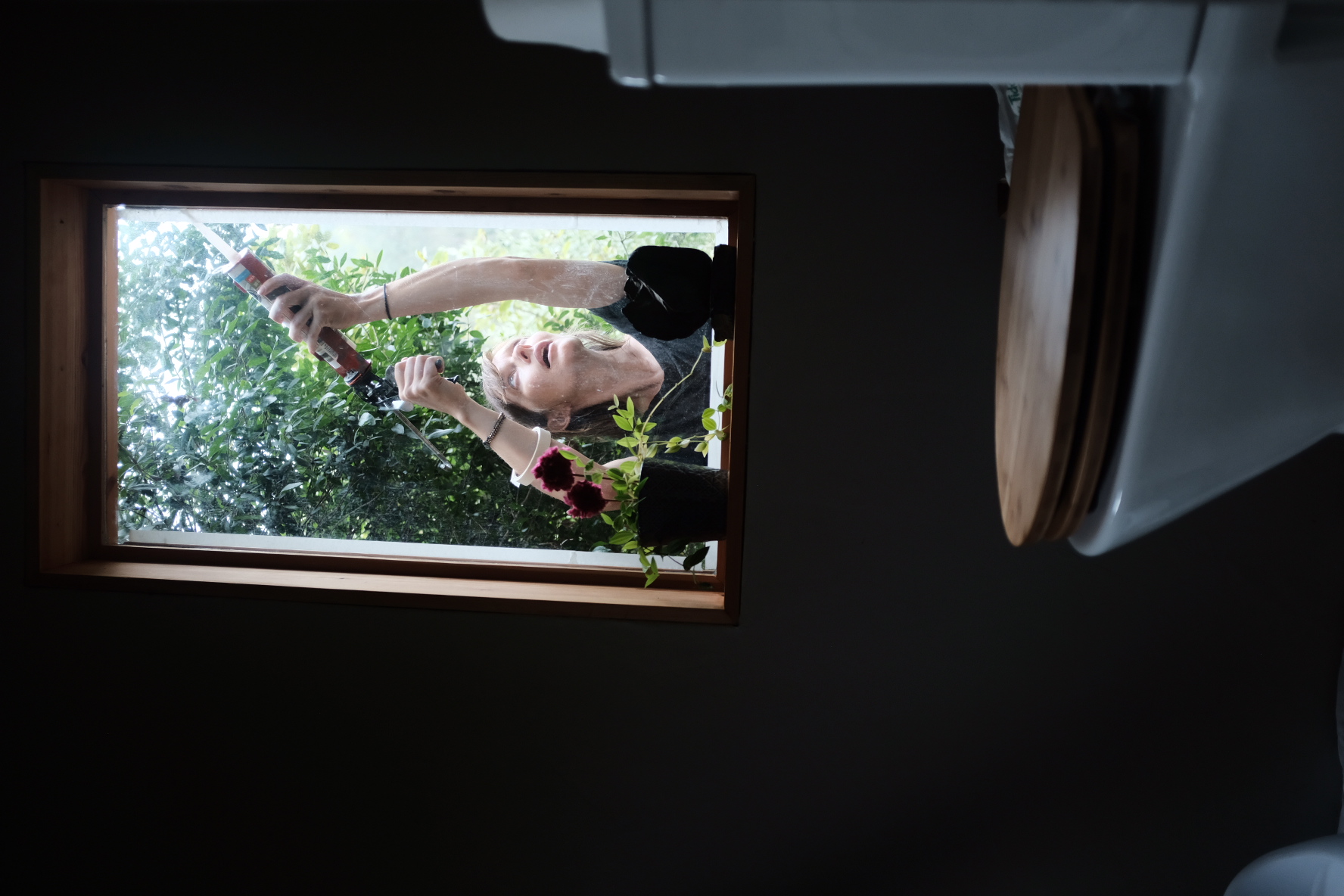 A woman seen through the bathroom window sealing the frame from outside