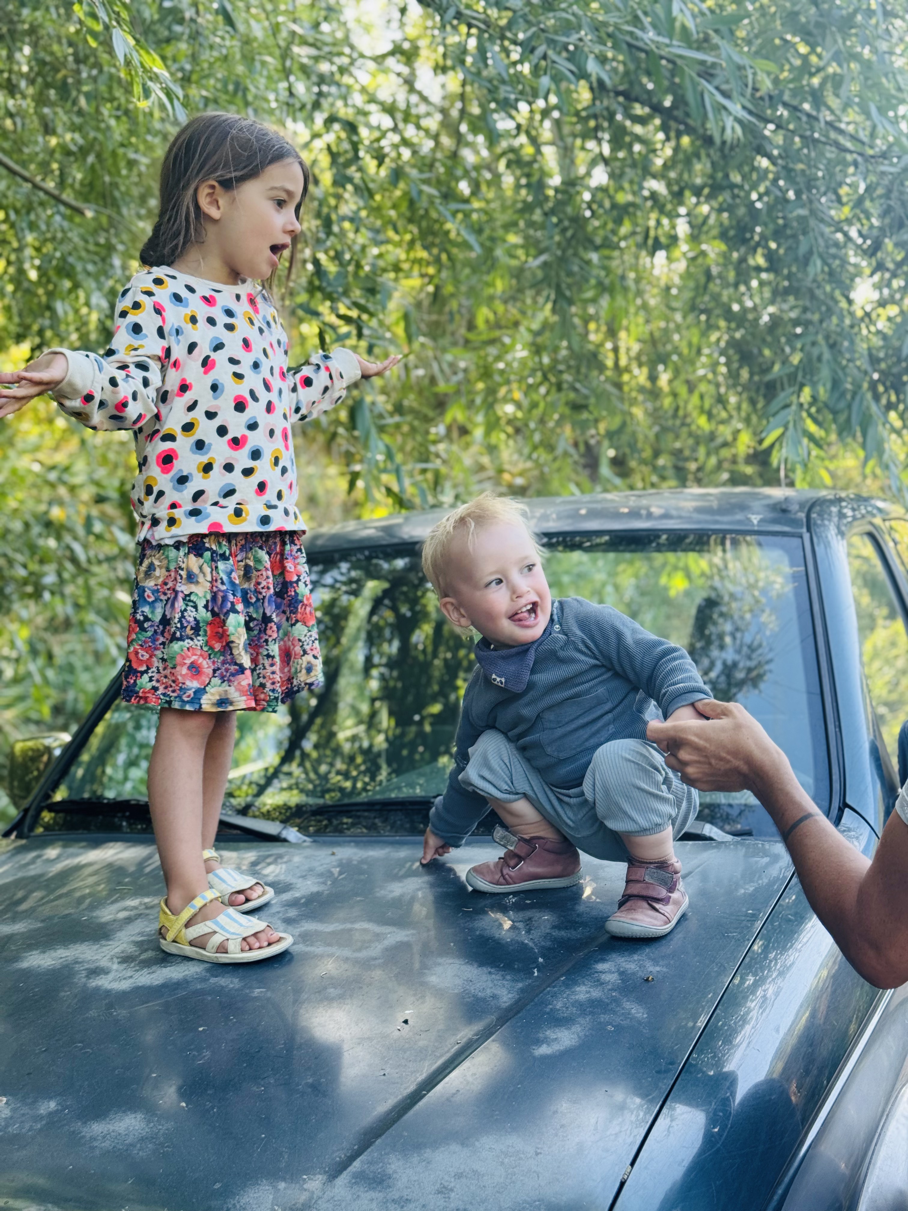 Two children standing on the bonnet of the old car under the willow