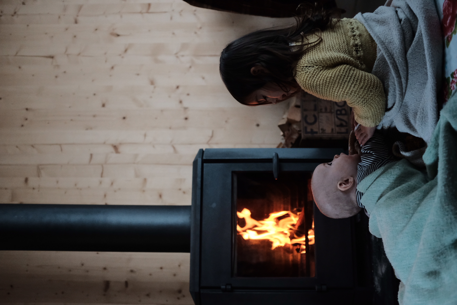 Two children wrapped in blankets watching the wood stove burn