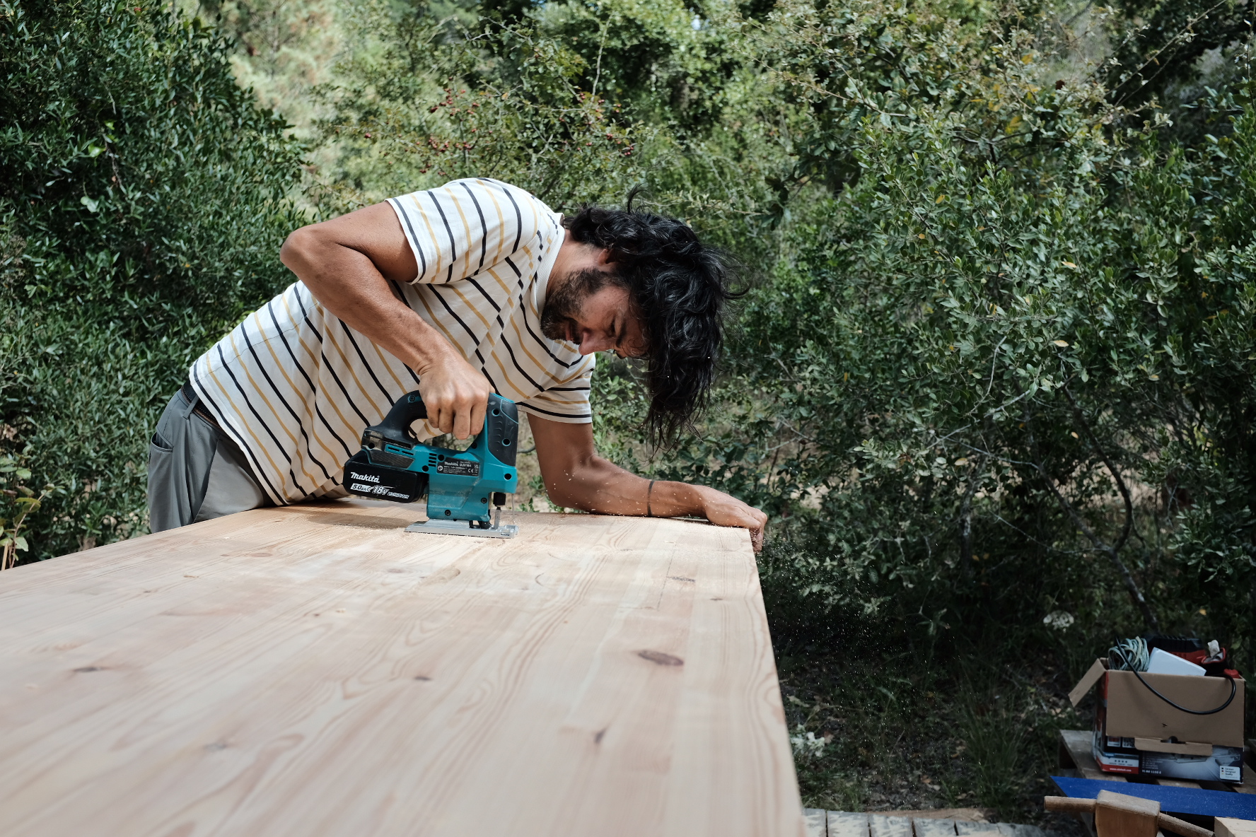 A man cutting a large pine counter top with a jigsaw outdoors