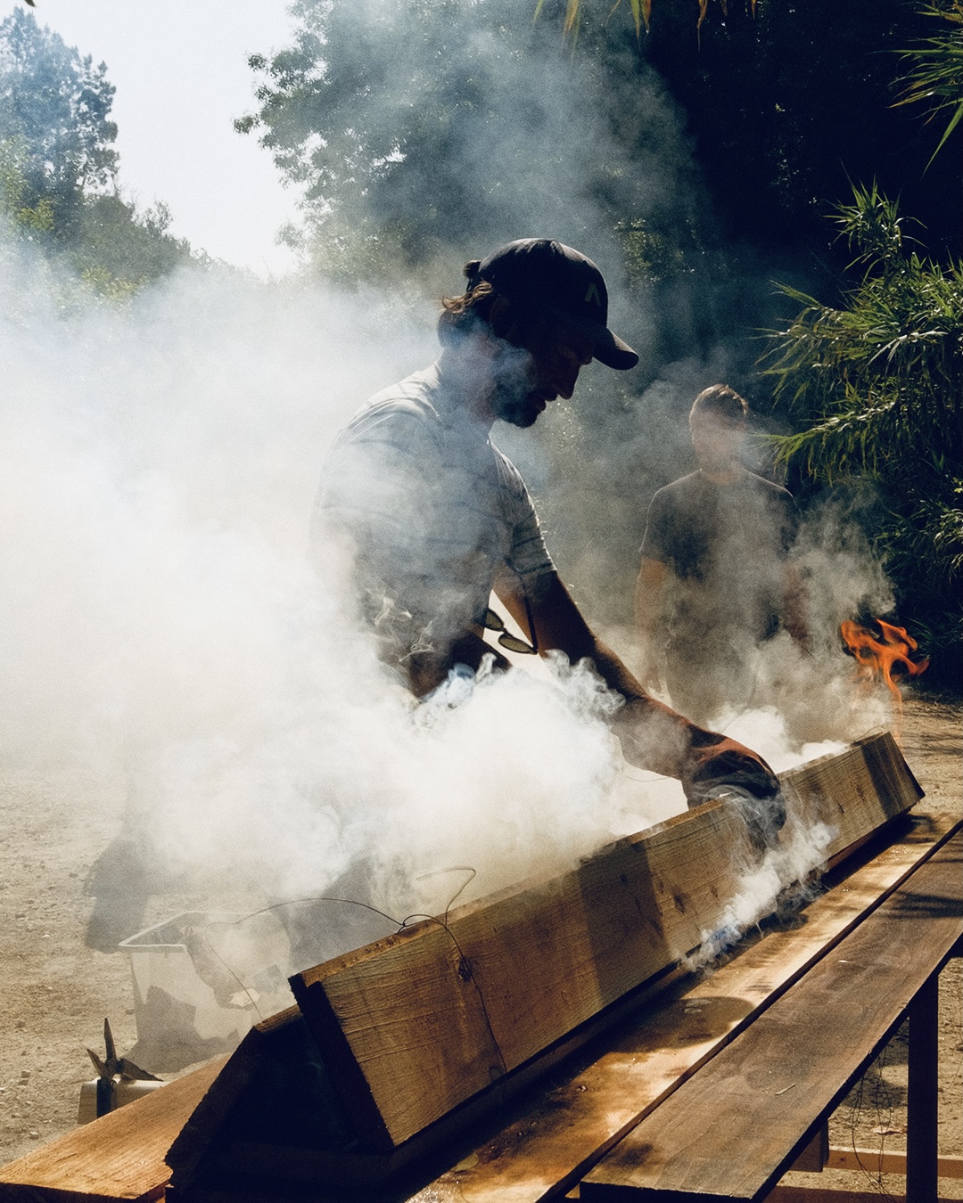A man wiping down a smoking charred beam in a cloud of smoke