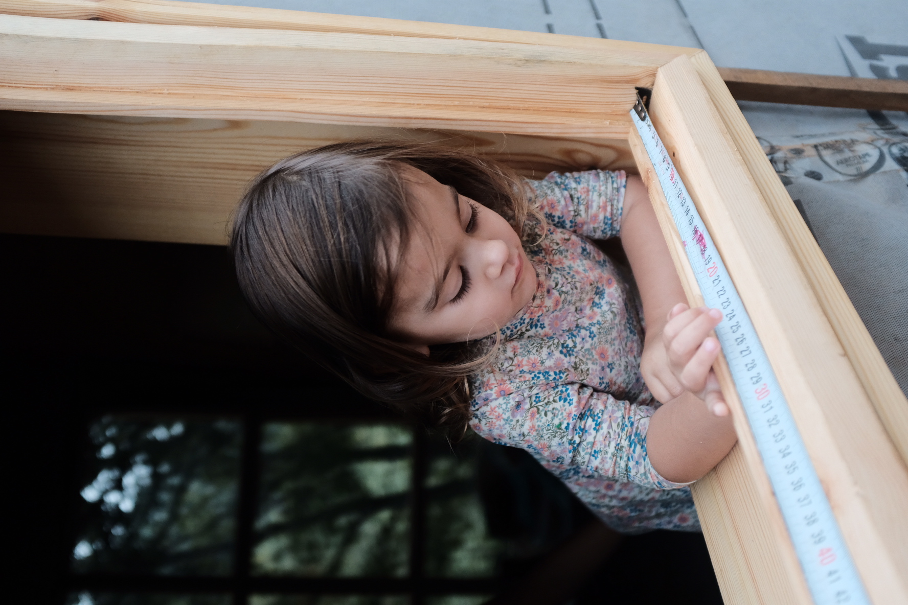 A small girl leaning on a new window sill with a tape measure