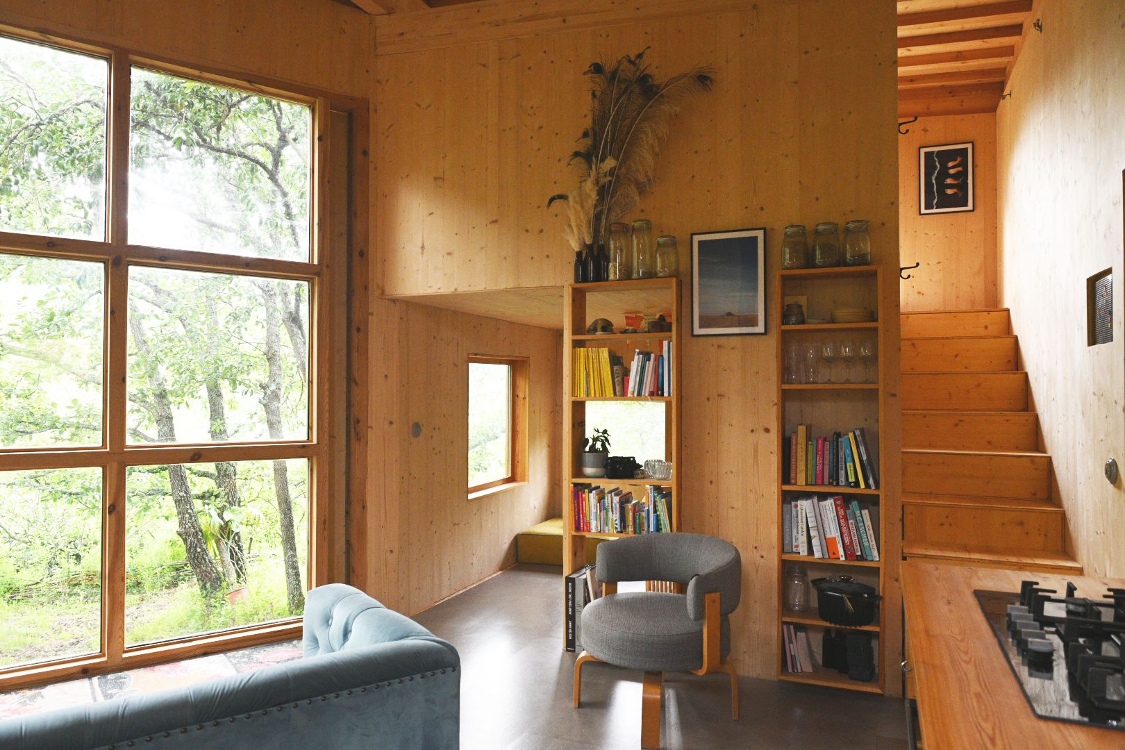 Dining nook with a grey armchair and timber bookshelves filled with books and jars