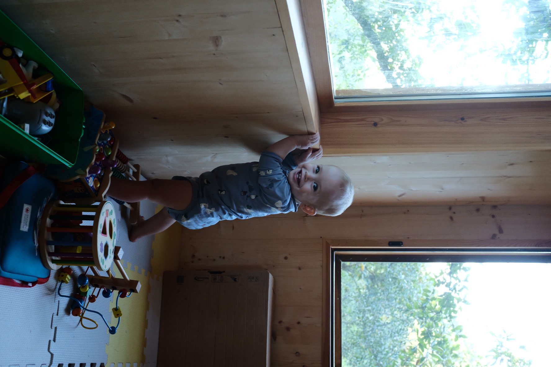 A smiling baby pulling himself up at the playroom window