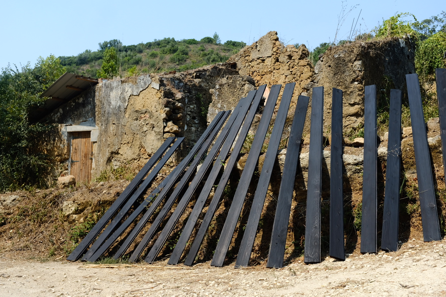 Charred black cladding planks leaning against an old stone ruin in the sun